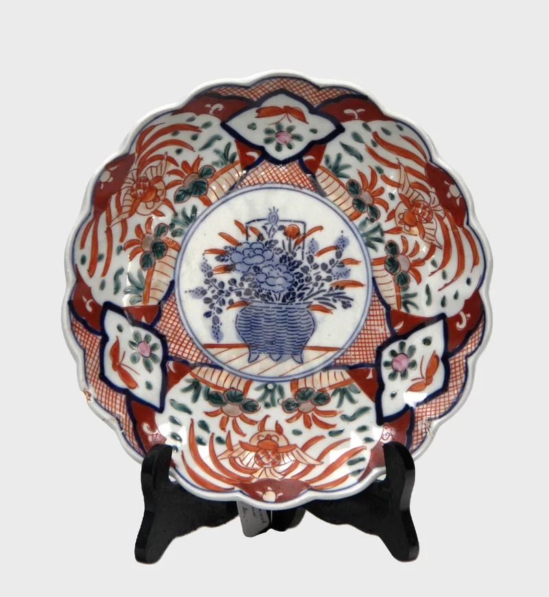 Imari bord (10) - Porselein › Borden - €20.00 - Bord met gelobde rand met centraal motief van bloemenmand en blauwe versiering op de achterrand.
21.5cm diameter.
19e eeuw