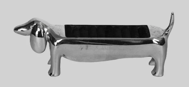 Ringenhouder - Zilver › Diversen - Verzilverde ringenhouder in de vorm van een dashond.
Op de rug een geplooid kussentje waar diverse ringen kunnen tussengestoken worden.
14cm lang.
Vintage