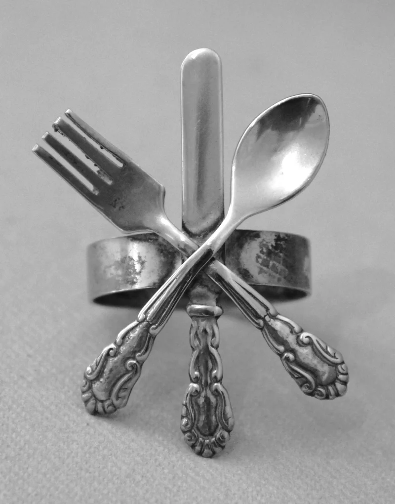 Servietring - Zilver › Serviesgoed - €15.00 - Servietring met versiering van bestekmotief.
Verzilverd met veel slijtage, zichtbare onderliggende messing drager