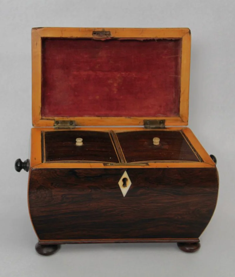 Theekistje in palissanderhout - Diversen › Dozen en theekistjes - Sarcofaagvormig theedoosje in palissanderhout en afboordingen in satijnhout. Binnenin voorzien van twee compartimenten, elk afgedekt met een dekseltje in palissanderhout en een knopje in ivoor.
22 x 13cm, 16cm hoog
Georgean periode, ca 1820
Gepolitoerd op oude wijze